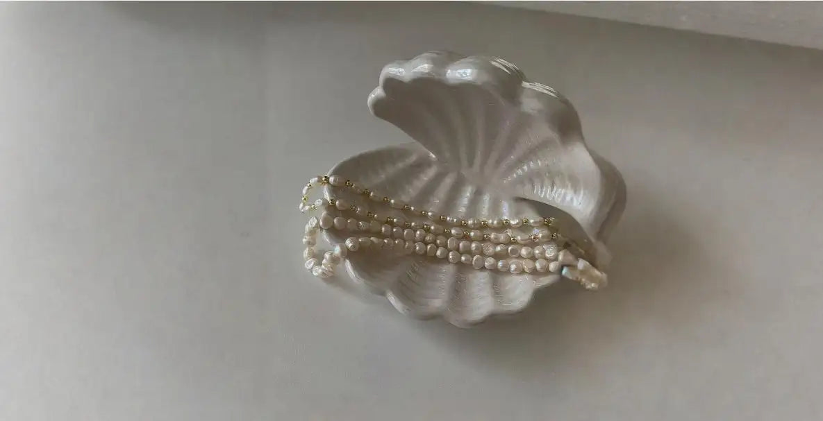 En delikat vit keramisk snäckskalformad prydnadsskål som håller flera rader pärlhalsband.