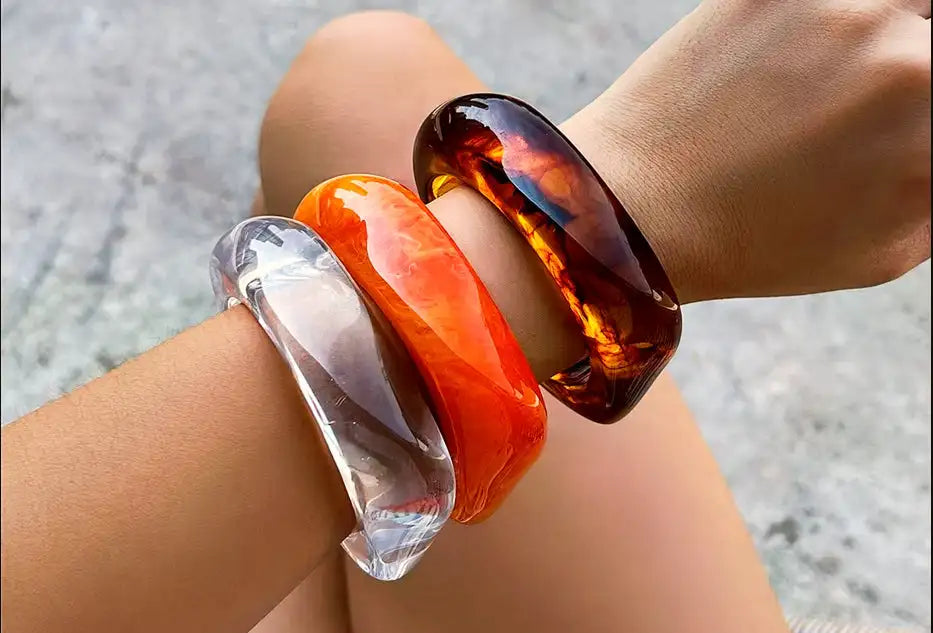 Tre glansiga, genomskinliga armband i klara, livfulla orange och bärnstens virvelmönster.