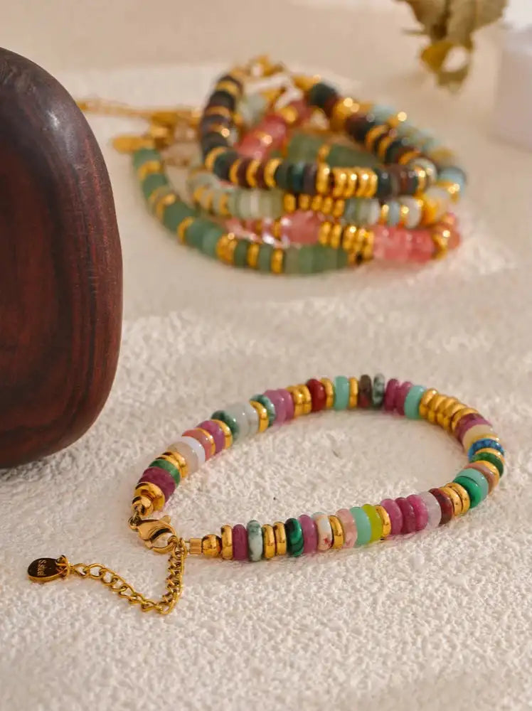 Ett livligt, flerfärgat pärlarmband med alternerande ronder av rosa, gröna, gula och guldfärgade pärlor med en matchande guldfärgad spänne.