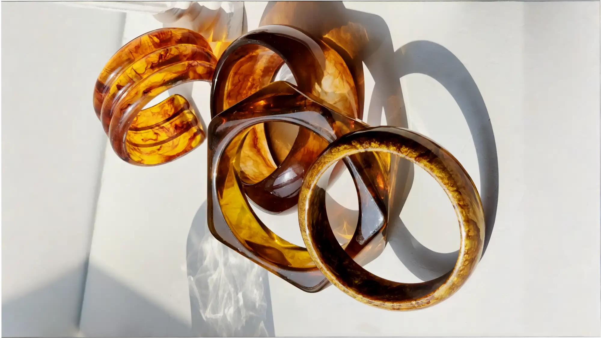 Ett set av bärnstensfärgade, genomskinliga resin-armband med virvlande marmorerade mönster och släta, polerade ytor.