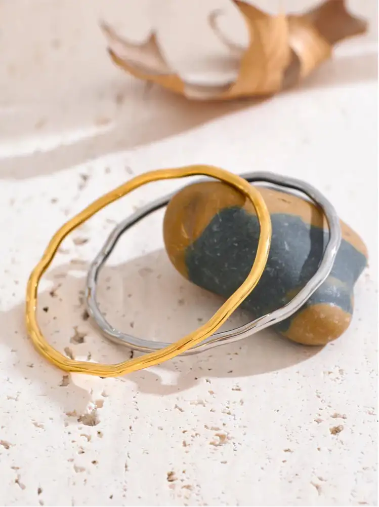 Två staplade armband, ett med en texturerad guld finish och det andra i slät silver.