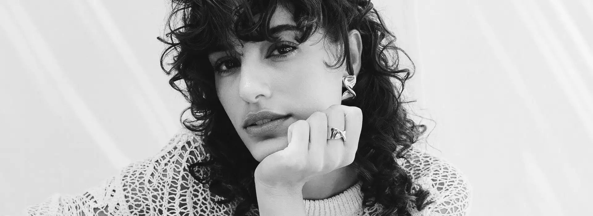 Svartvit porträtt av en kvinna med lockigt hår som bär en intrikat spetströja.